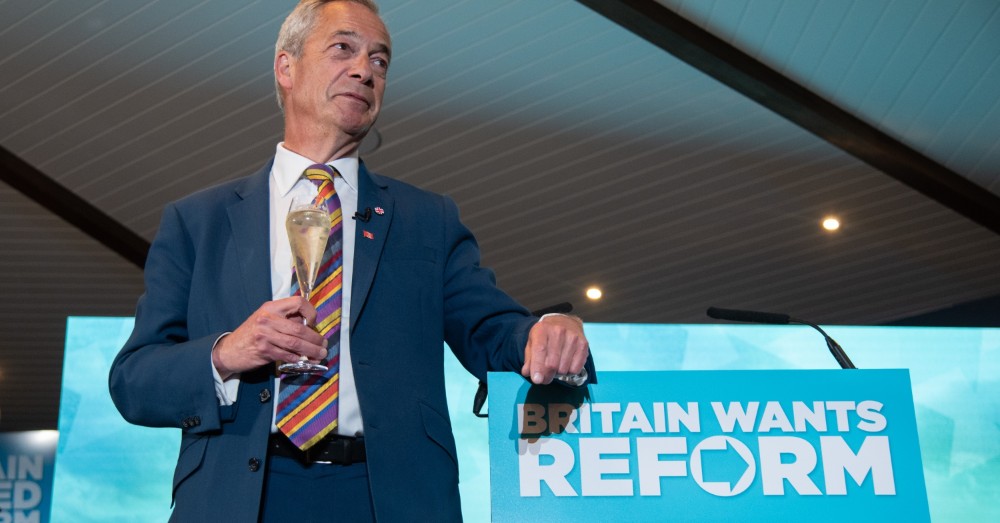 Nigel Farage met een glas in de hand bij een spreekgestoelte met Britain Wants Reform