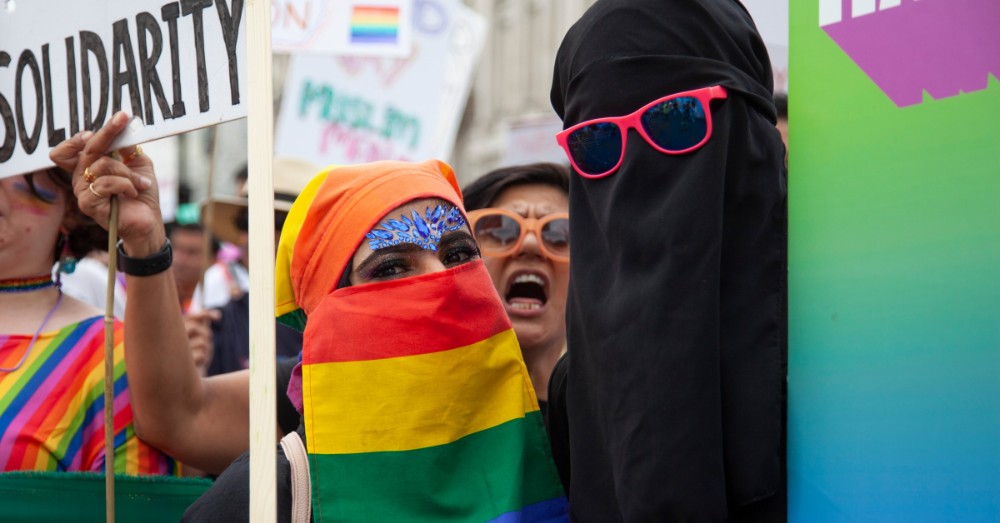 Twee vrouwen met nikab, waarvan één in regenboogkleuren, op een Pride-mars